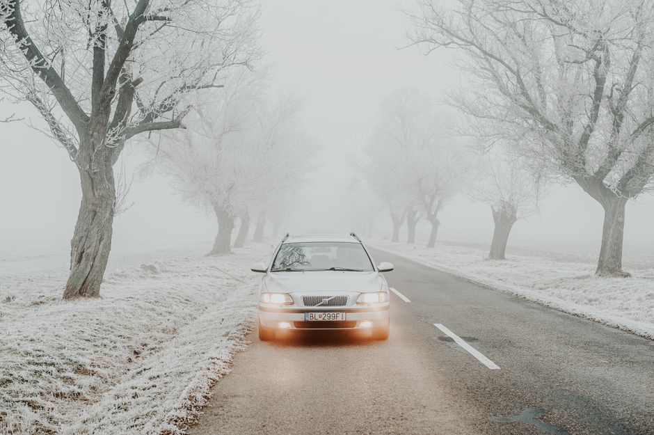 A car travels on a foggy winter road lined with frost-covered trees in Slovakia.