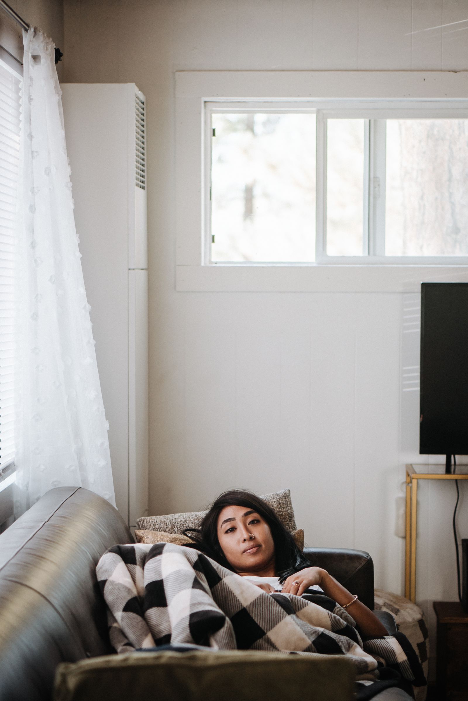 A woman resting on the sofa wrapped in a cozy blanket, easing the discomfort of luteal phase bloating before her period
