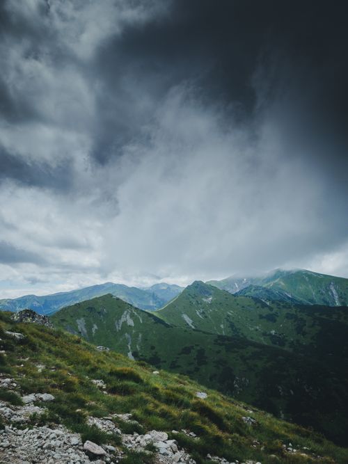 Free Scenic view of towering mountains under a dramatic sky with dark rain clouds. Stock Photo