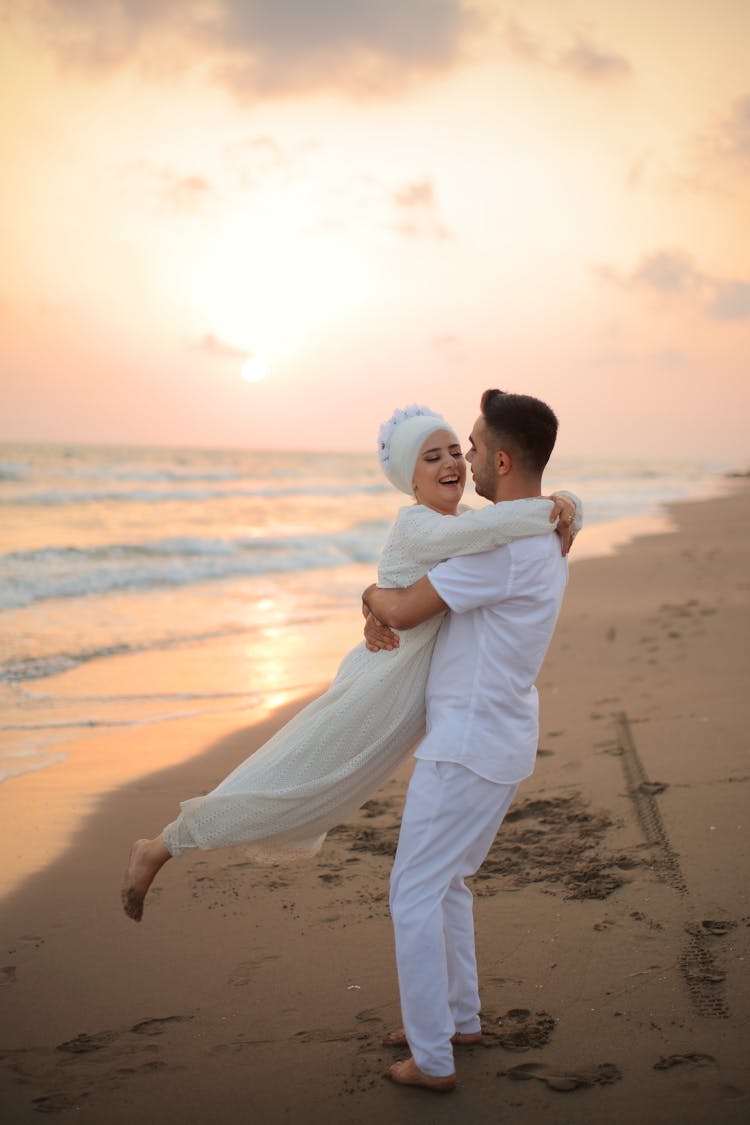 Man Hugging Smiling Woman On Beach At Sunset