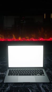 A blank laptop screen on a marble table with a fiery background, offering dramatic contrast.