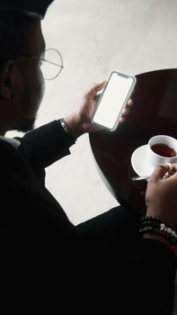 An adult man holding a smartphone and coffee in an indoor setting. Close-up shot.