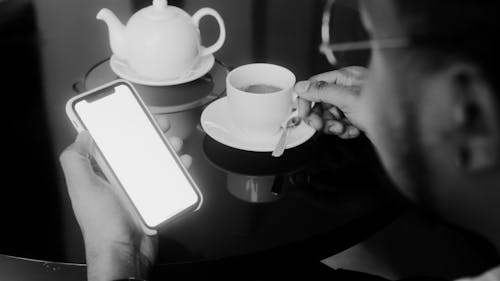 Man Using a Cellphone and Holding a Cup of Coffee