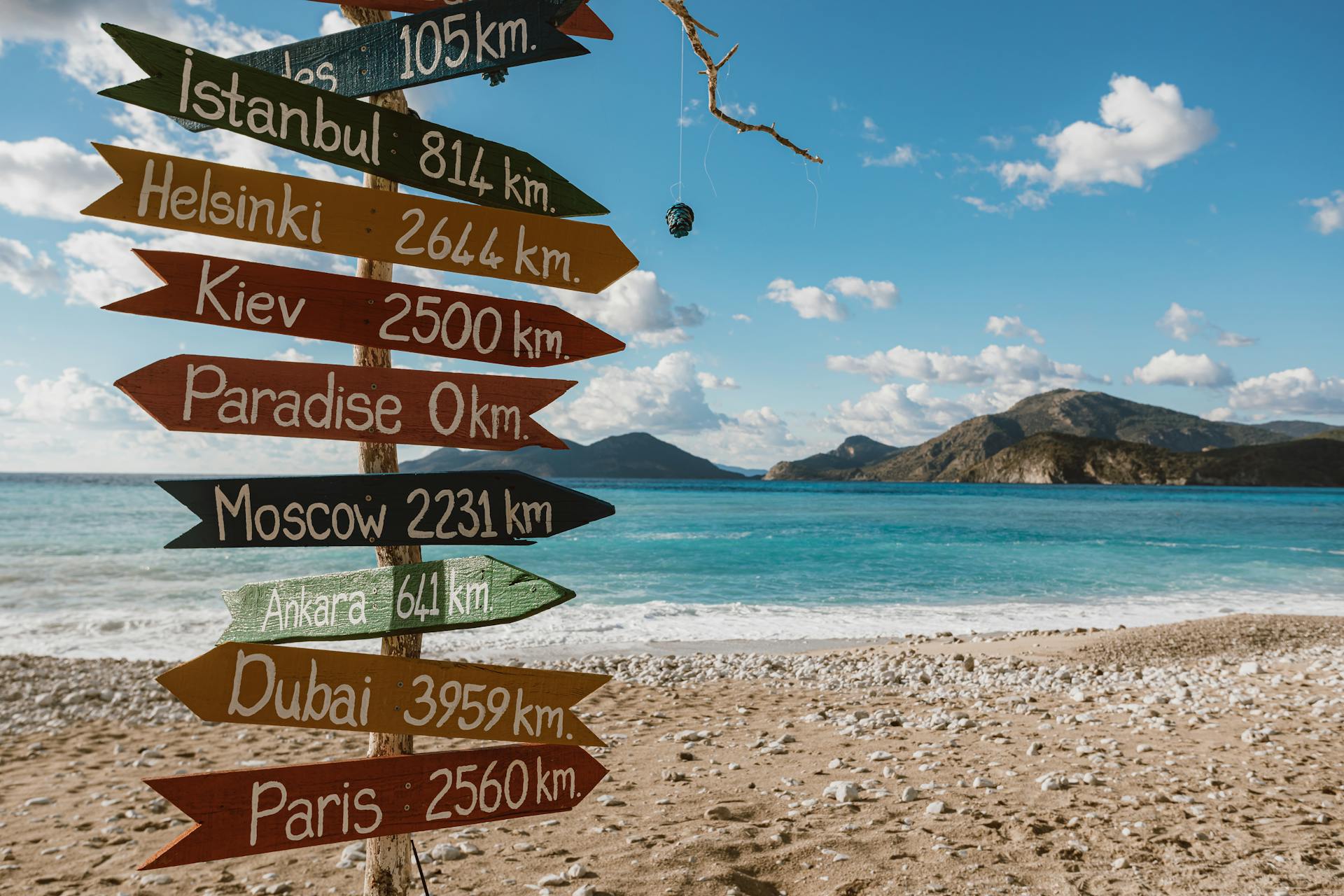Colorful signpost on beach showing distances to various cities, sunny day.