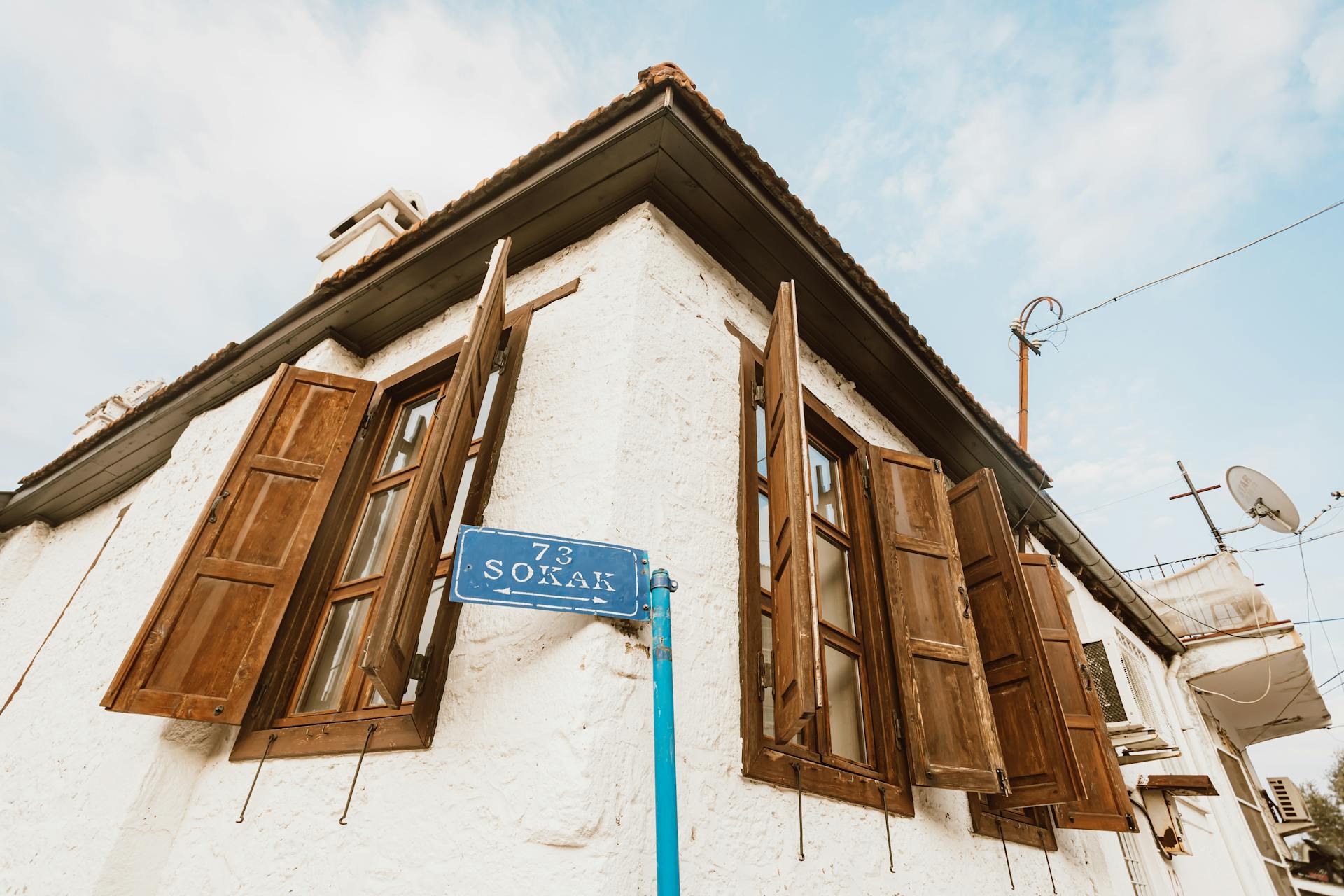 Rustic corner building with wooden shutters and street sign under a clear sky.