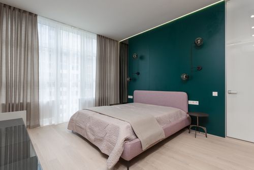 Free Comfortable bed with small round bedside tables placed in modern room with chiffon curtains and green wall decorated with creative lamps Stock Photo