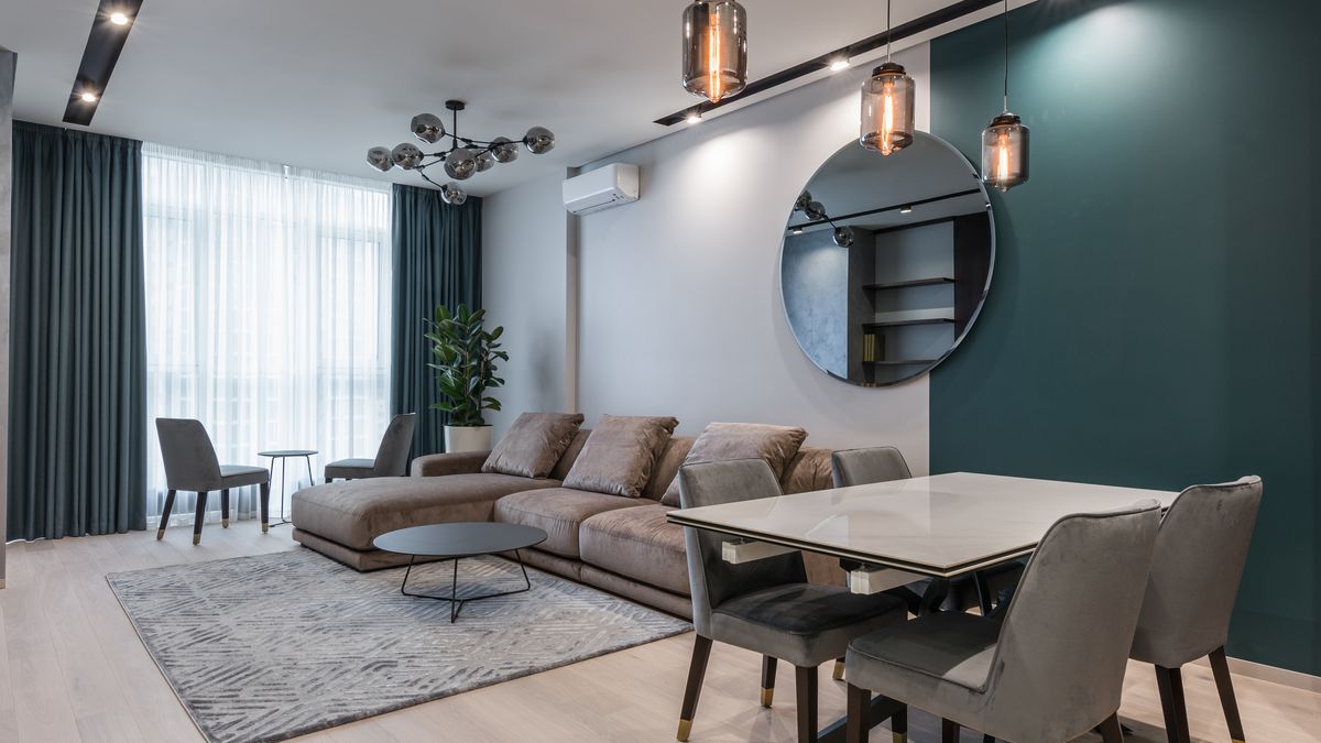 Interior of modern living room with comfortable big sofa and dining zone decorated with creative lamps and mirror in daylight
