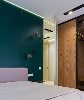 Comfortable bed with coverlet placed near wooden wardrobe in modern apartment in daylight