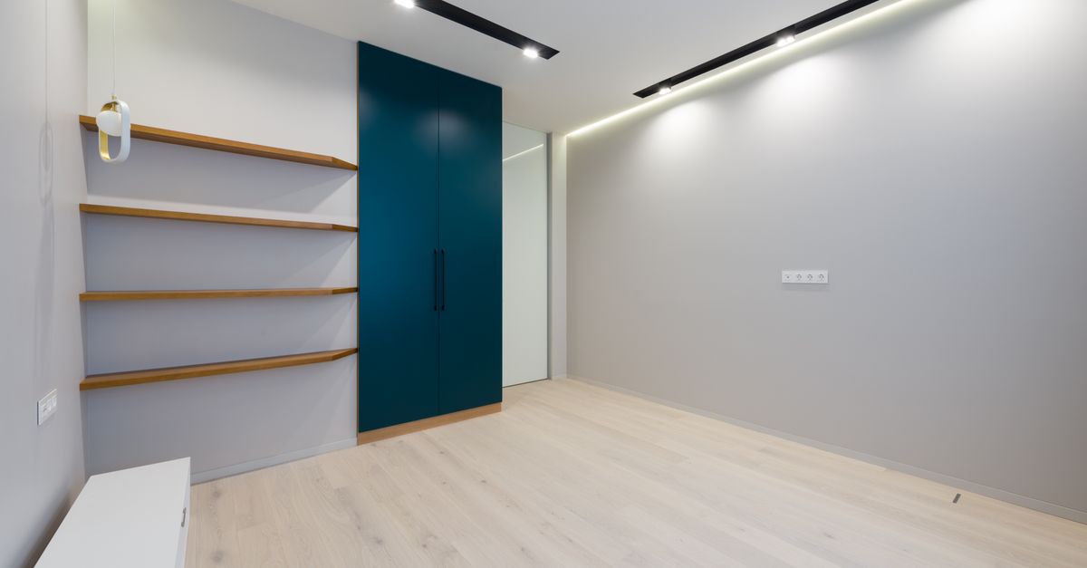 Wooden shelves and wardrobe placed in spacious modern room with laminate floor and bright glowing lamps