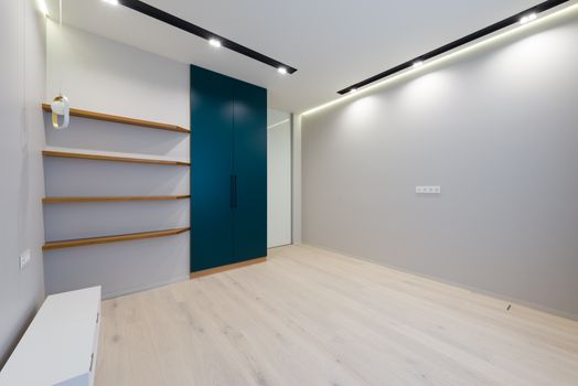 Wooden shelves and wardrobe placed in spacious modern room with laminate floor and bright glowing lamps