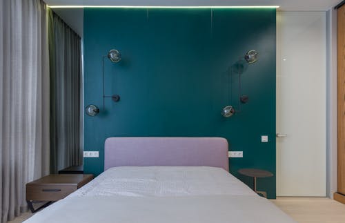 Interior of contemporary bedroom with mirror hanging near comfy bed placed near green wall decorated with creative lamps