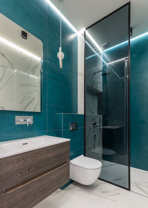Interior of modern bathroom with glass shower cabin ceramic sink and mirror hanging on blue tiled wall