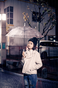 Portrait of a young woman with an umbrella during a rainy night, wearing a beanie and looking up.