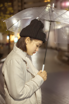 Side view of a young woman with an umbrella during a rainy night on a city street.