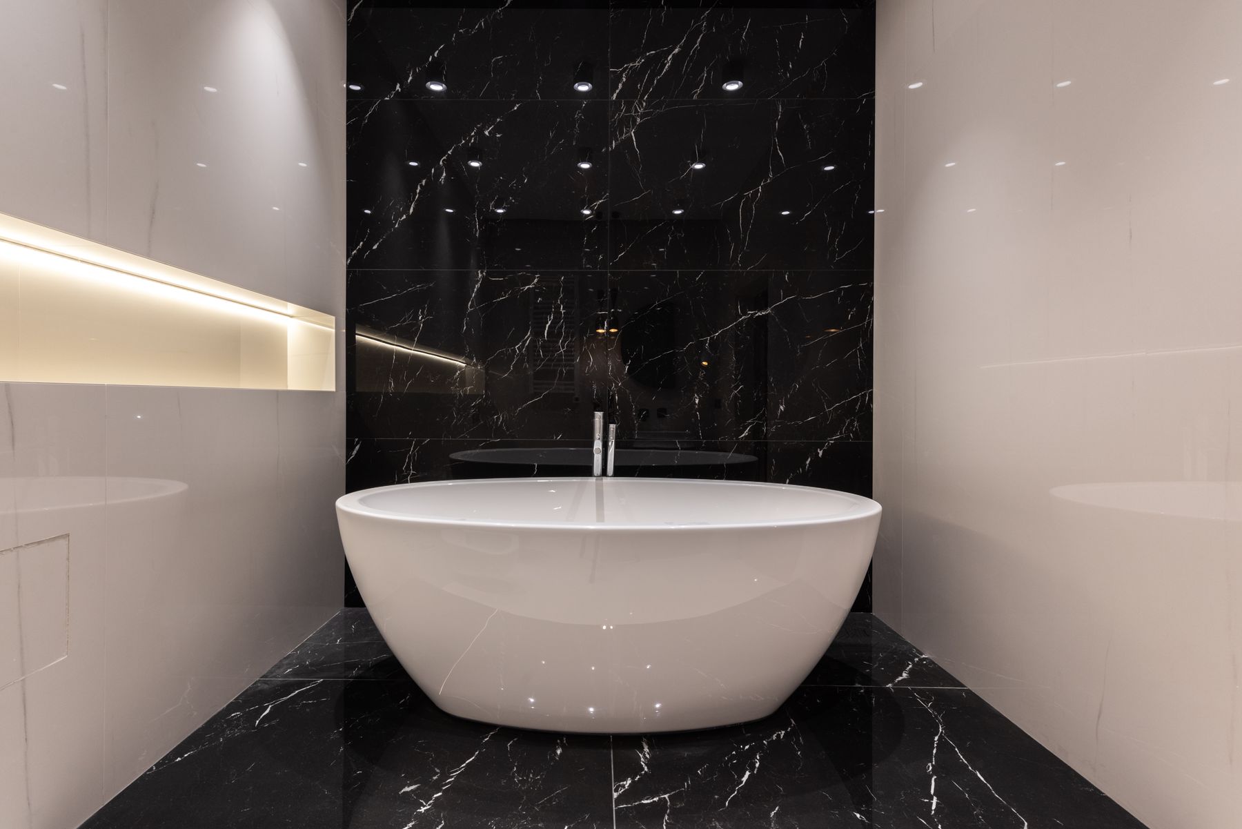 Black-led modern bathroom with dark marble, soaking bath and strong material contrast