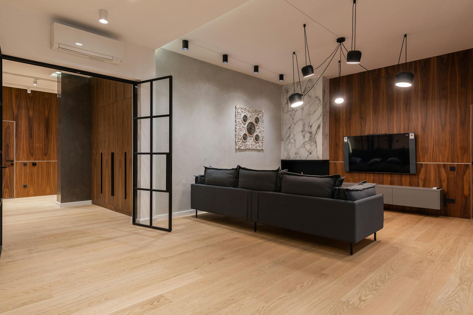 Interior of spacious modern living room with comfortable sofa and TV set hanging on wooden wall under loft styled lamps