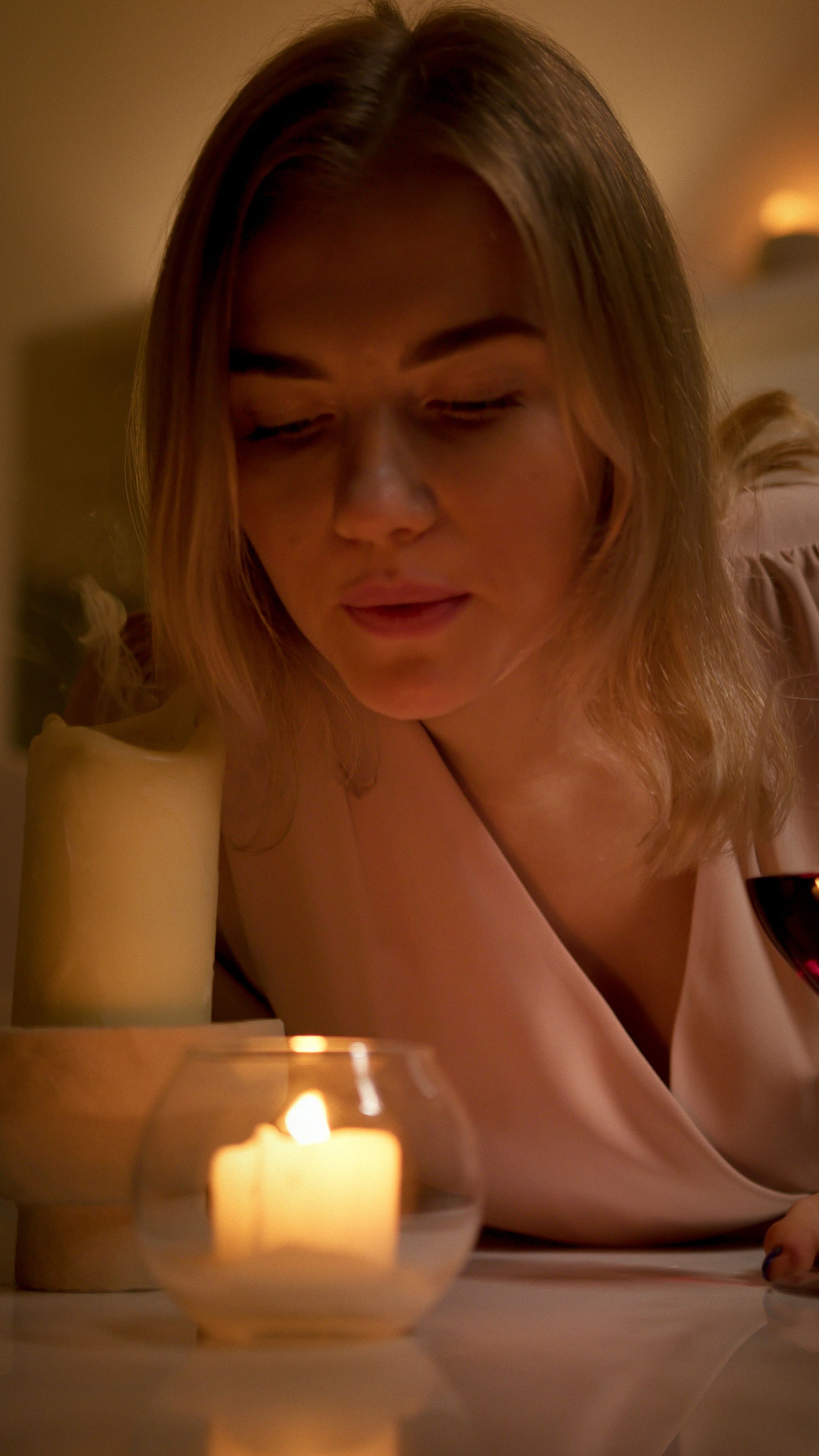 A woman looks thoughtfully at glowing candles, creating a peaceful indoor atmosphere.