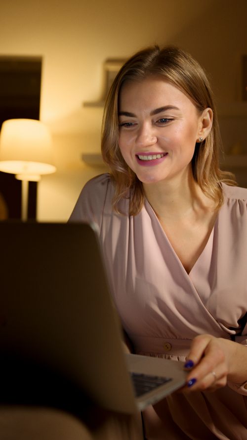 Free A woman smiles while browsing on her laptop in a cozy indoor setting at night. Stock Photo
