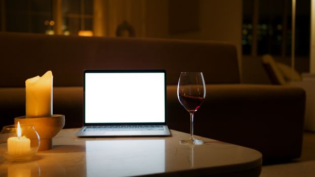 An inviting indoor scene with a blank laptop screen, candles, and a glass of red wine on a table.