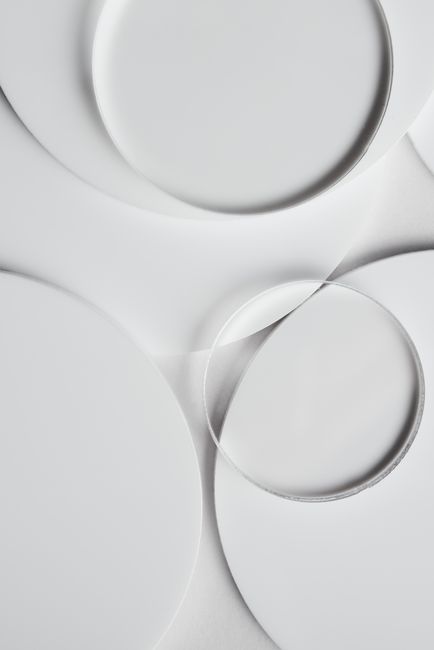 Minimalist composition of overlapping round glass plates on a white surface.