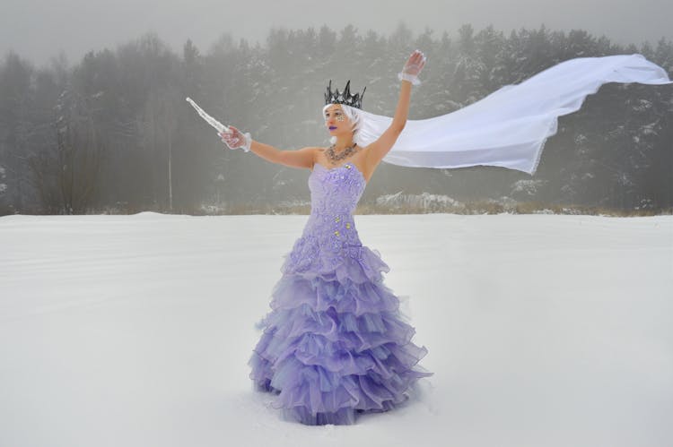 Woman In Crown And Dress With Icicle On Snowy Meadow