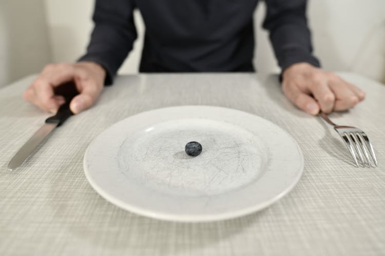 Person Sitting At Table With One Berry On Plate
