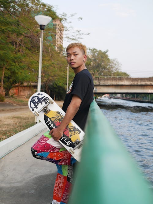 A Man in Black Shirt and Colorful Pants Holding a Skateboard