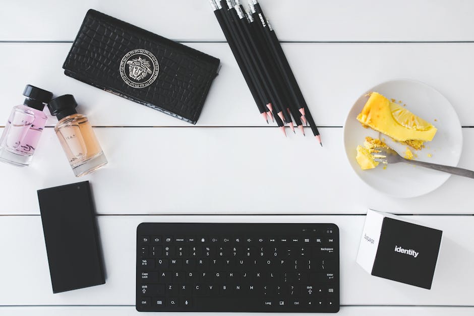 How Password Managers Generate and Store Unique Passwords Securely Flat lay of a modern workspace with keyboard, perfume, cake slice, and stationery on white desk.