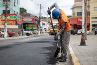 A construction worker paving a street in Cotia, Brazil, using a shovel during the day.