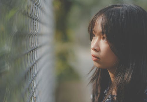 Side view of serious ethnic girl with long dark hair and brown eyes looking through metal fence