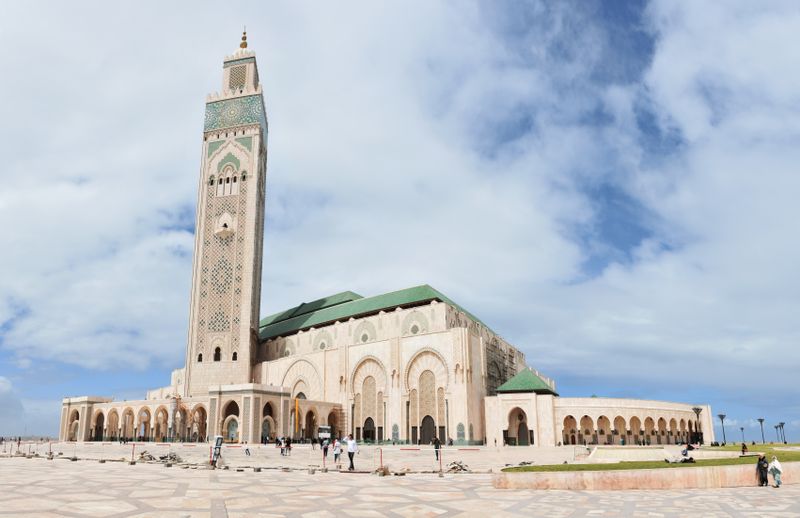 The Hassan II Mosque and its tall minaret on the Casablanca waterfront under a blue sky with clouds.
