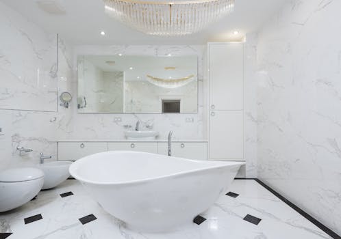 Elegantly designed white marble bathroom featuring a modern freestanding tub and chandelier.
