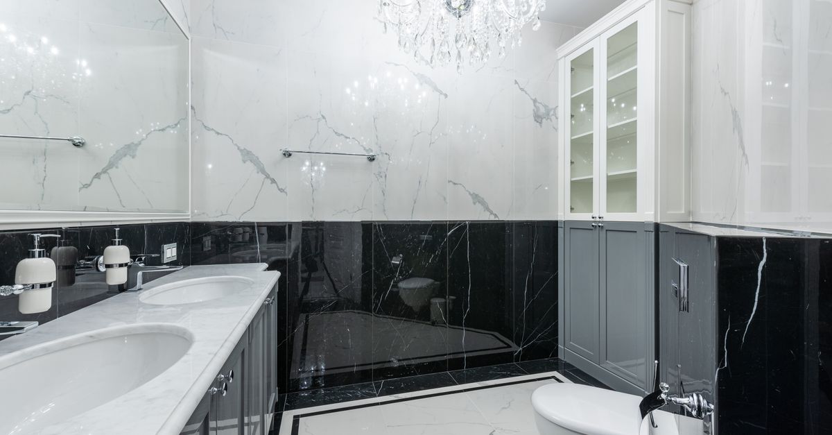 Interior of convenient modern bathroom with white clean sinks and toilet under glowing chandelier