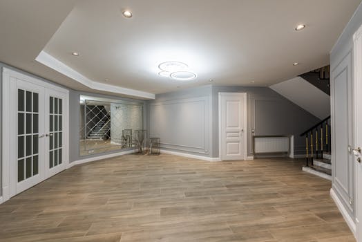 Interior of spacious empty hall with white doors next to mirror in front of staircase with railings in modern light house