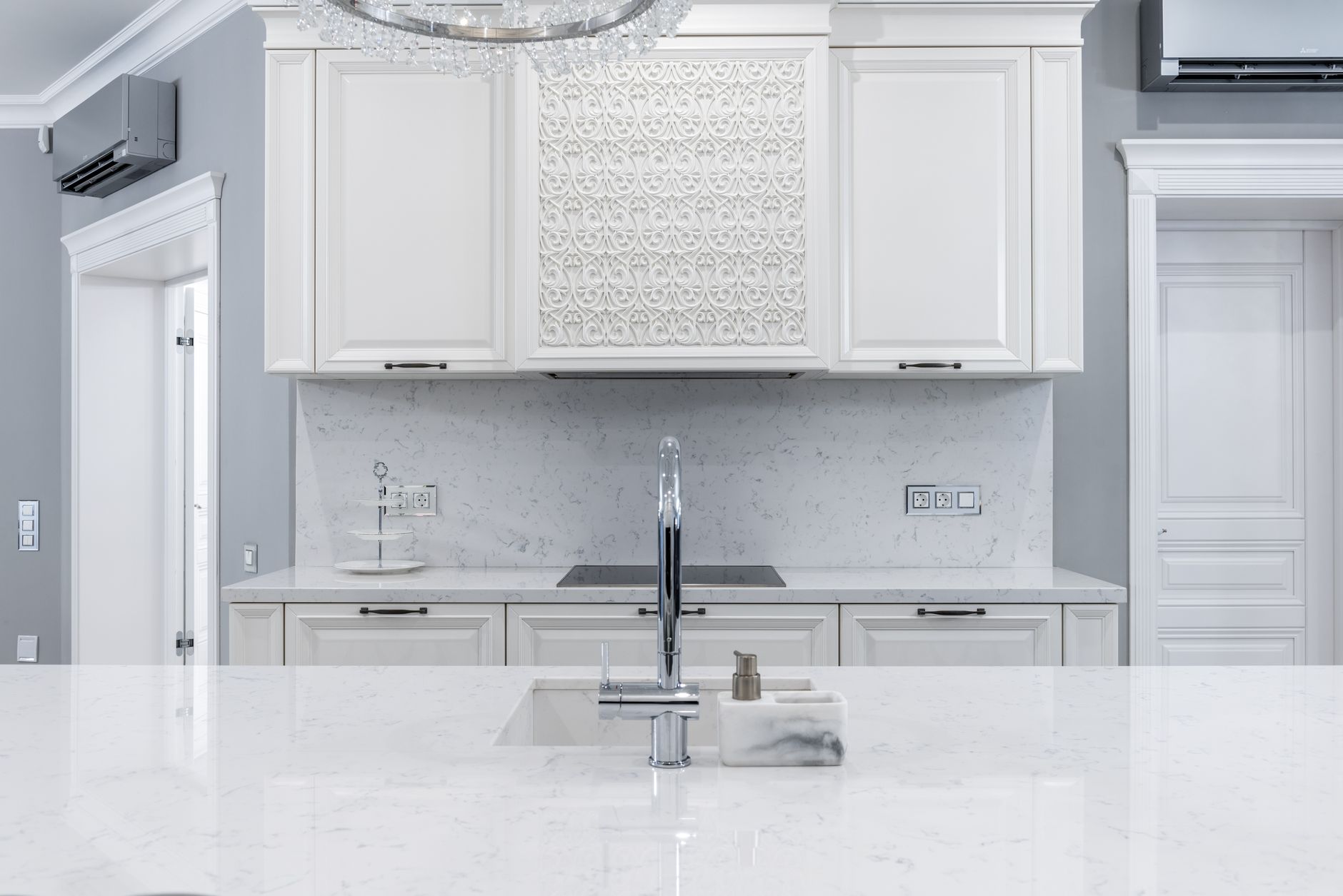 Interior of white classic kitchen with marble counter and chrome faucet.