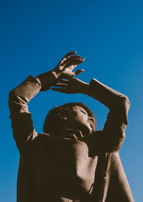 Free Low-angle shot of woman posing against a clear blue sky with raised hands and a contemplative expression. Stock Photo