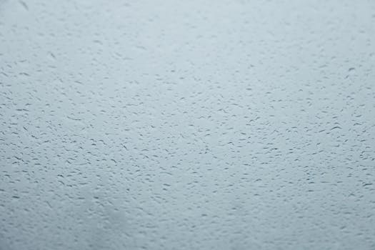 Detailed view of raindrops on glass, creating a textured pattern with natural light.