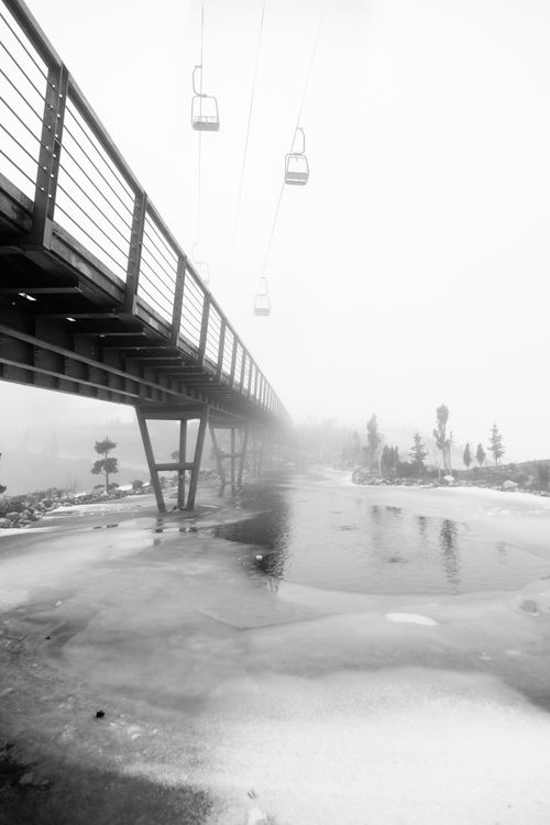Free A dramatic black and white winter scene of a bridge and cable cars over a frozen river. Stock Photo