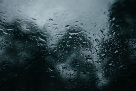 Raindrops on a glass window with a blurred, moody background, capturing the essence of a rainy day.
