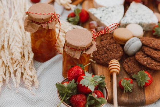 Delightful spread of homemade jam, strawberries, cheese, and cookies on a picnic table.