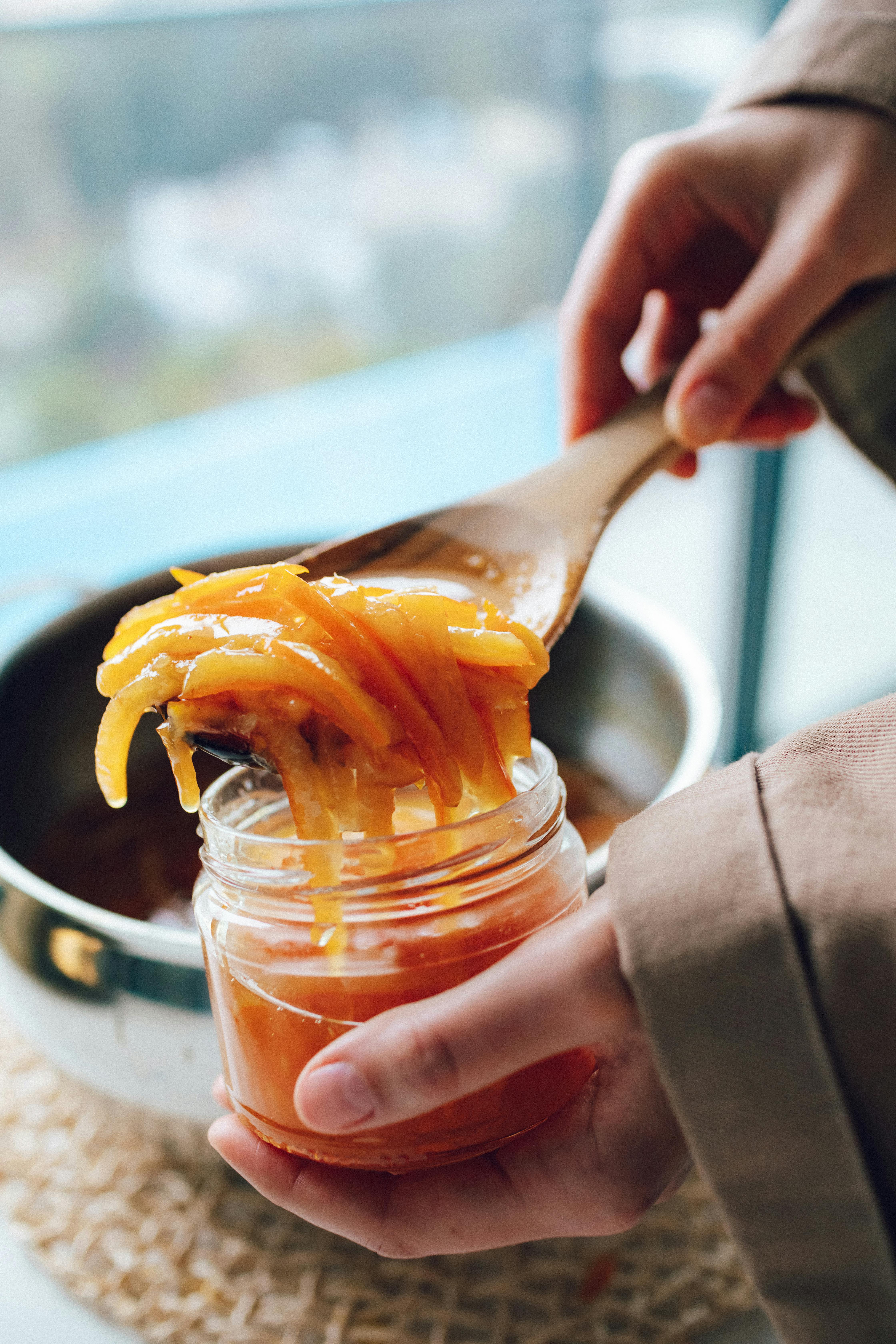 woman holding a spoon and a jar of homemade orange jam
