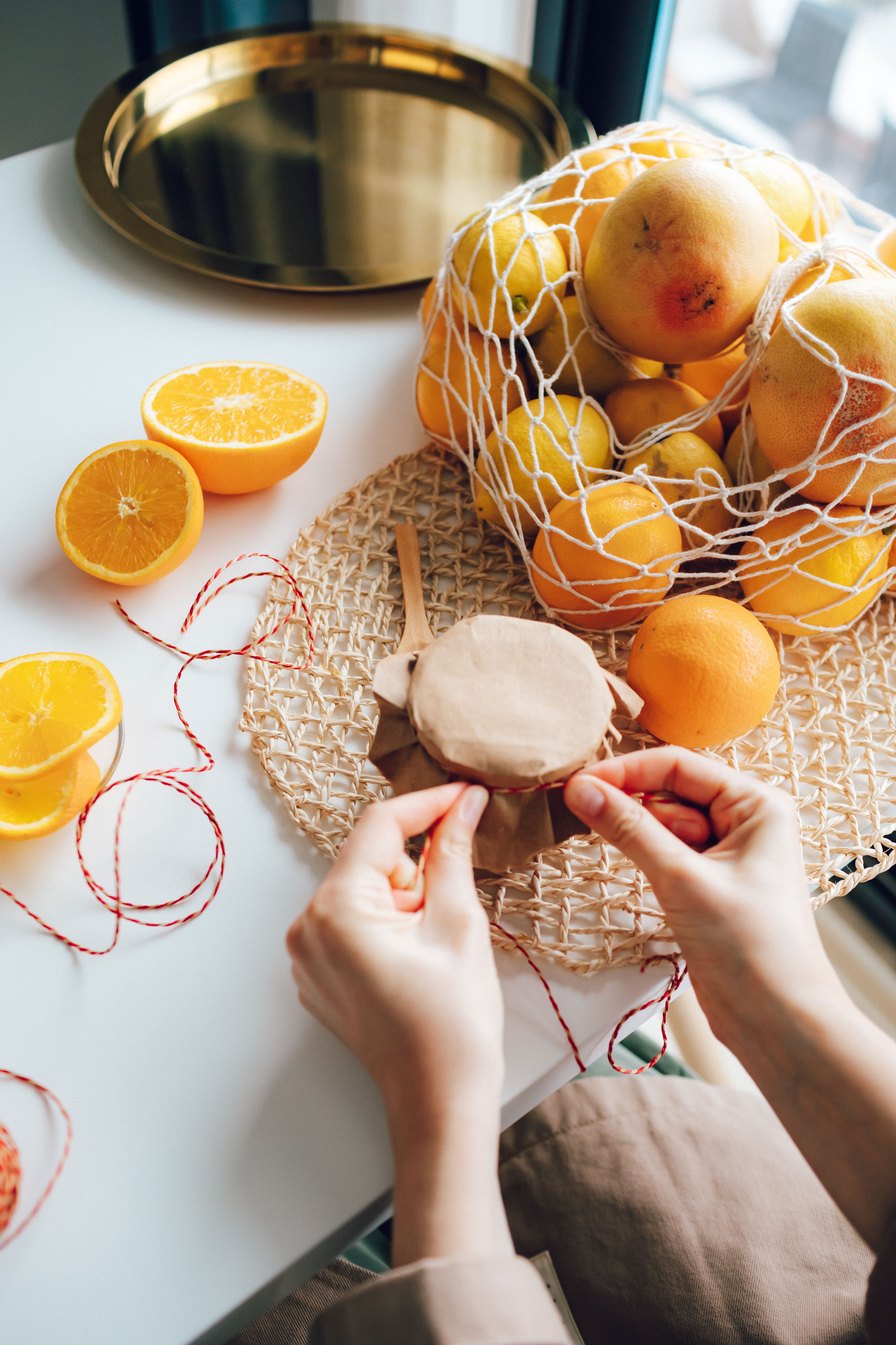 Hands wrapping homemade orange jam jar with citrus fruits and thread in cozy kitchen.
