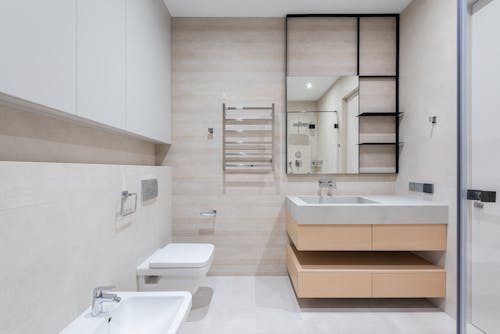 Interior of modern light bathroom with bidet and toilet next to sink with cabinet under mirror