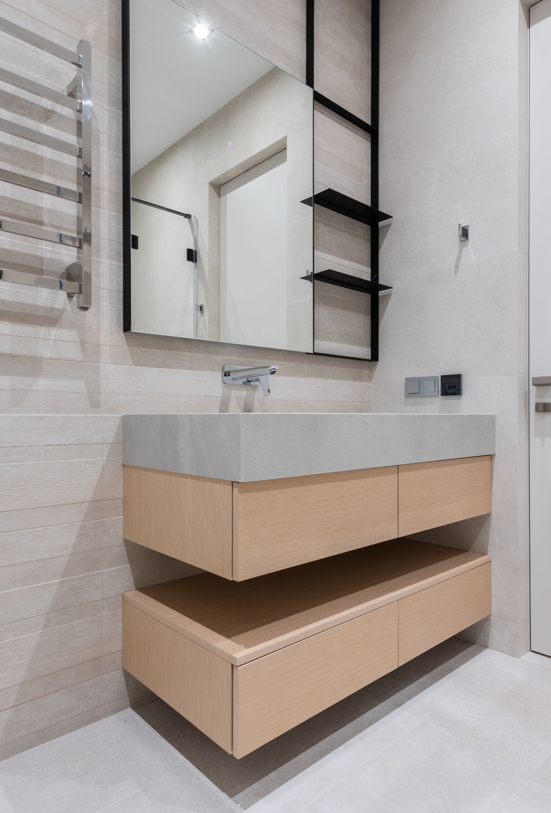 Floating pale timber vanity with two broad drawers, a white basin, large mirror and black open wall shelves