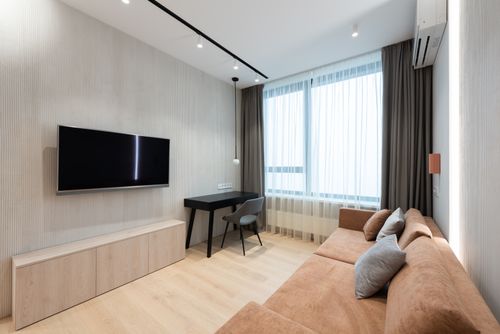 Free Interior of modern living room with sofa with pillows and TV on wall next to table with chair and curtains on window Stock Photo