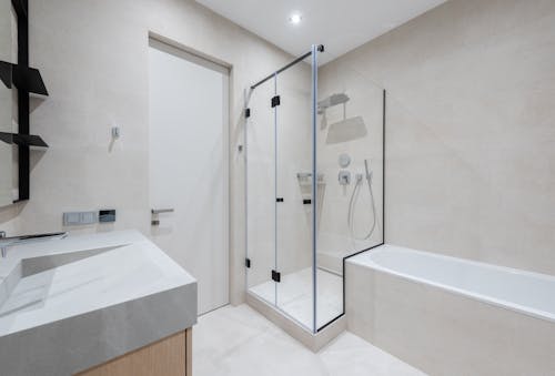 Interior of modern light bathroom with bathtub and shower next to sink with cabinet near door