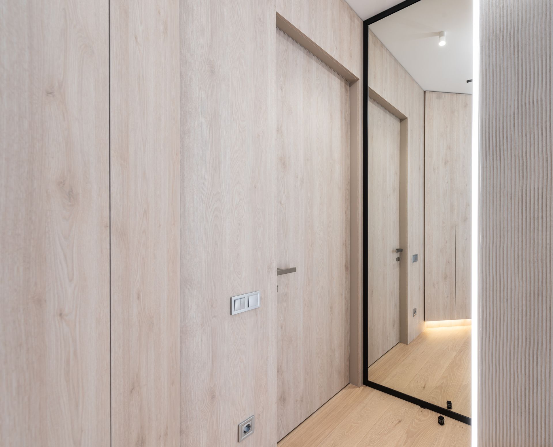 Bright and modern minimalist hallway with wooden features and large mirror reflection.