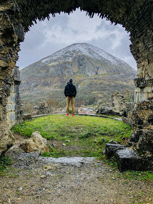 Free A Back View of a Person Standing Near the Archway while Facing the Mountain Stock Photo