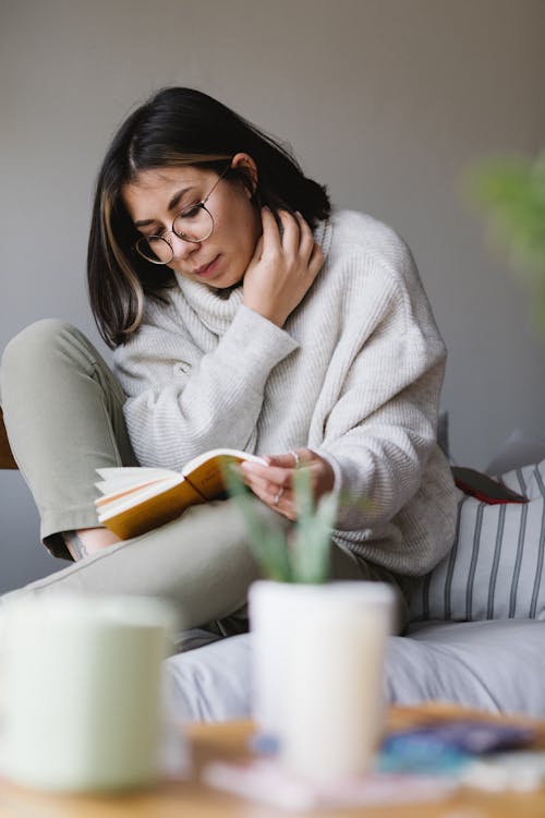 Free Focused young woman reading interesting novel on couch at home Stock Photo