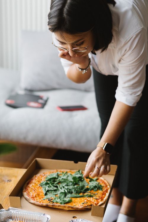 Free From above of crop young hungry lady opening box with appetizing takeaway pizza while standing in living room during weekend at home Stock Photo